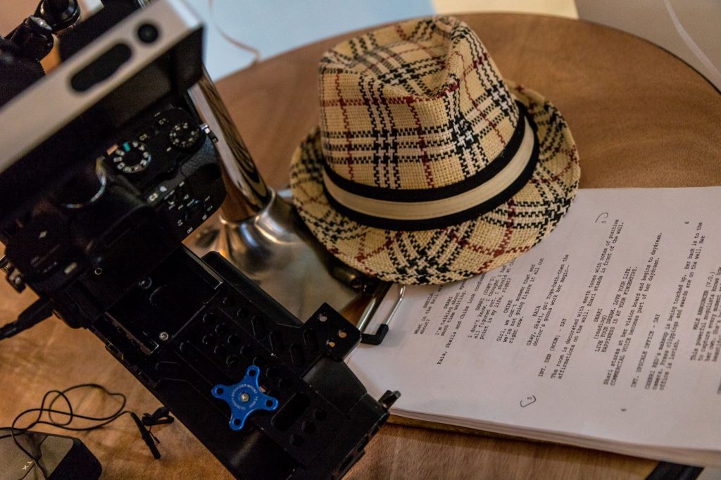 A wooden table with a hat, a camera and some paperwork on it.